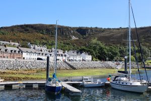 White painted houses on Shore Street Ullapool from the harbour with boats on the water on a sunny day.