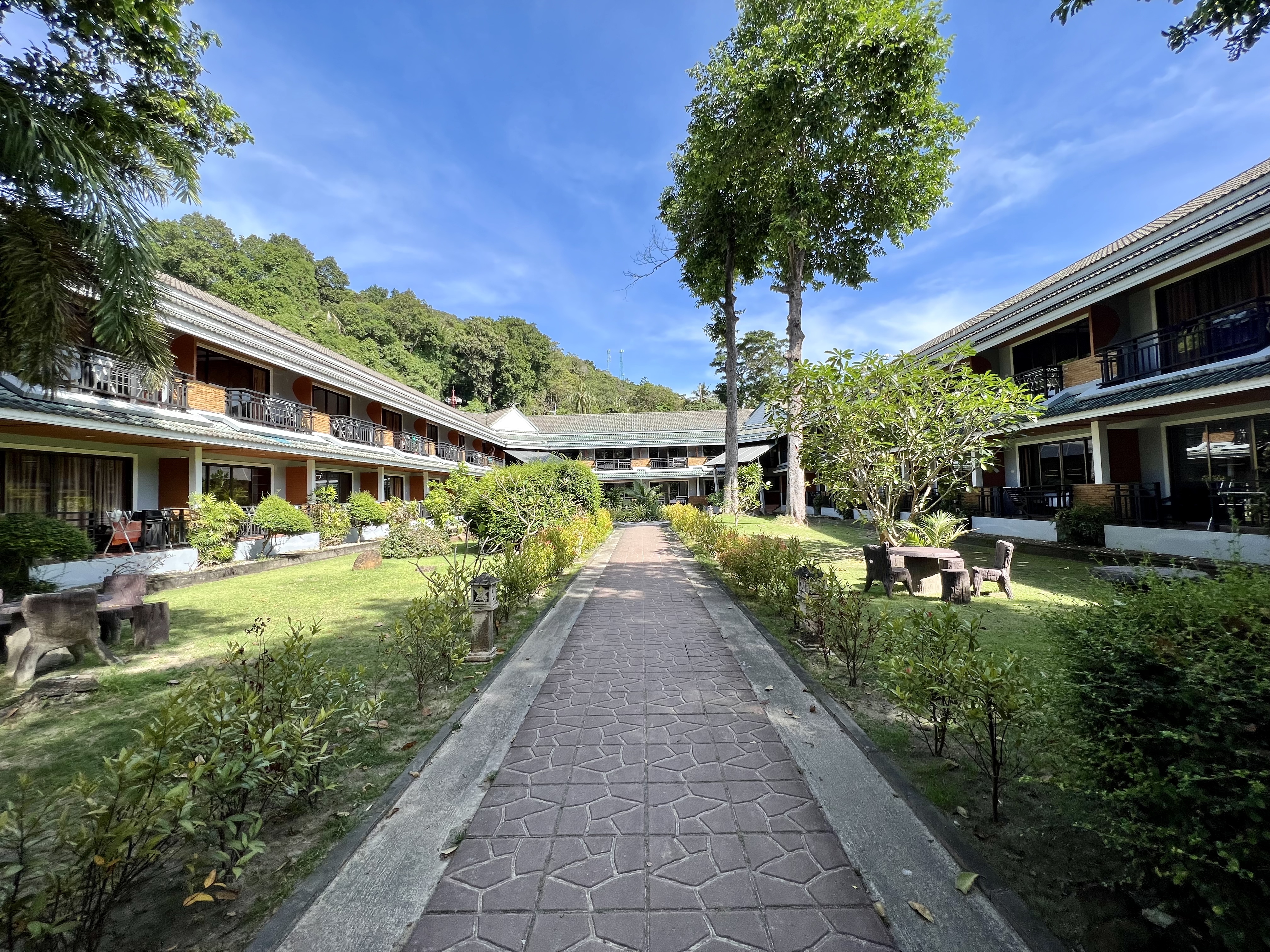 A stone walkway through a grassy courtyard surrounded by a two-story building complex with balconies.

