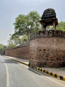 Stone fort wall with domed chhatri watchtowers lining a curved roadside, captured near Delhi’s historic fortifications.