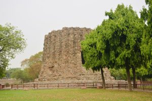 Side view of the unfinished Alai Minar near Qutab Minar, Delhi, with lush green trees adding beauty to the ancient stone structure.

