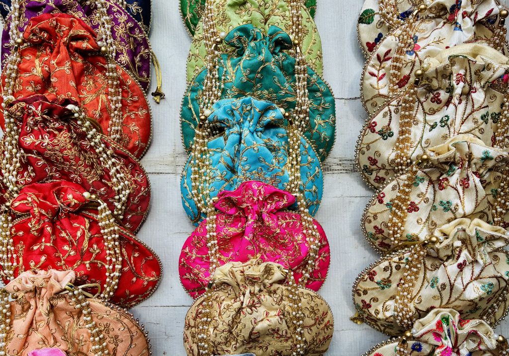 A collection of small traditional Rajasthani-style bags sold in Jaipur Johari Bazar. Each bag is adorned with intricate golden embroidery and embellished with strings of pearl-like beads.
