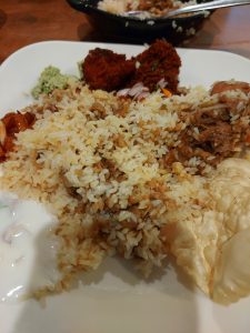 A plate of biryani is served with raita, papadam, and two small fried appetizers.