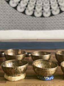 Several golden metal singing bowls are arranged on a wooden floor, some resting on decorative cushions.