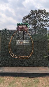 A decorative backdrop featuring a large, rounded frame adorned with faux flowers at the top. The frame has the word "Exceptional" displayed prominently in a stylish font.