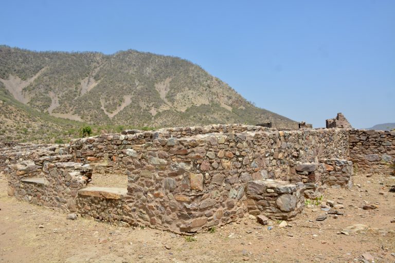 The weathered fortress wall of Bhangarh Fort, Alwar, Rajasthan, is set against the rugged landscape of the Aravalli Hills.