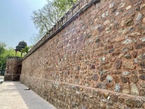 Long stone fort wall with a corner chhatri pavilion, built from mixed-color rocks, showcasing historic defensive architecture. Captured from Delhi.