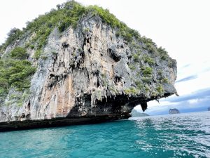A massive limestone cliff, known as a karst, rising dramatically from the turquoise sea in Thailand.

