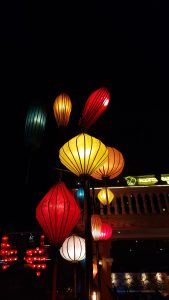 A nighttime shot of a variety of colorful, illuminated paper lanterns hanging from a pole against a dark sky.