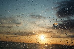 Sunset seen through a glass covered with water droplets, reflecting the cloudy sky and landscape