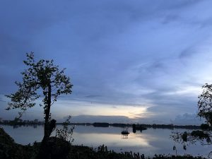 A tranquil body of water reflects the soft hues of twilight, with a partially clouded sky transitioning from blue to warmer tones at the horizon. 
