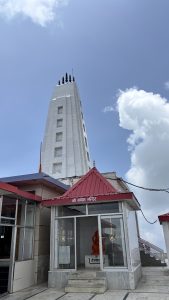 A tall, white Kali Timba temple tower stands against a blue sky with scattered clouds.
