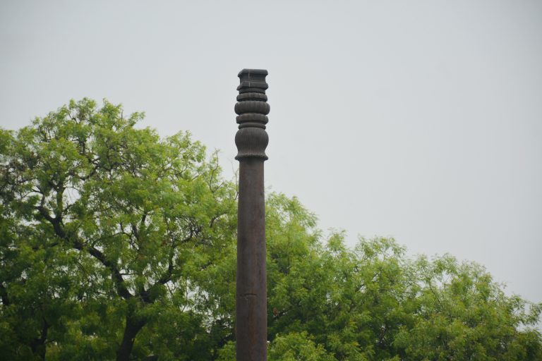 A detailed view of the top portion of the iconic Iron Pillar at the Qutub Complex, Delhi. Known for its rust-resistant composition, this ancient structure stands tall against a backdrop of fresh greenery, showcasing India’s rich metallurgical heritage.