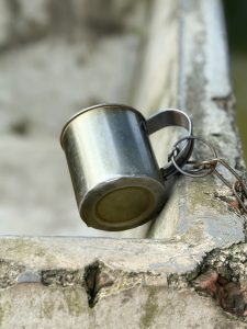 A close-up image of a metallic cup hanging from a chain on the edge of a weathered concrete surface.
