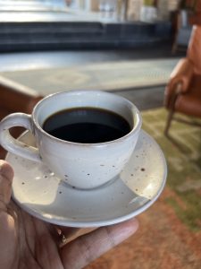 A hand holding a white ceramic cup and saucer filled with black coffee.