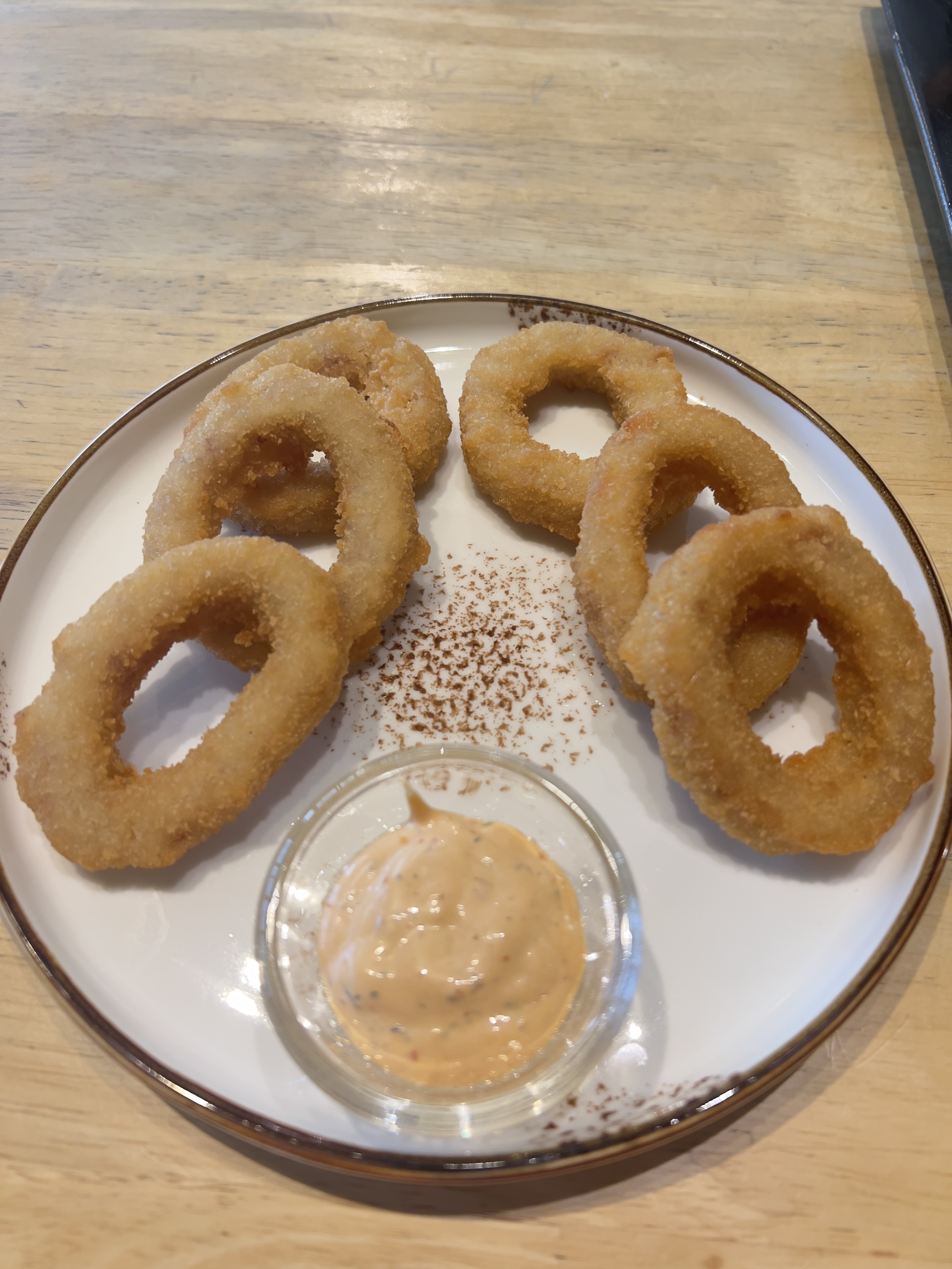 A plate of onion rings with a side of dipping sauce.