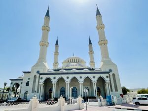 A large, white mosque with multiple domes and tall minarets under a clear blue sky.