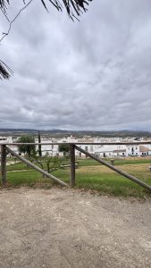 A scenic view showing white buildings nestled in a valley, surrounded by rolling hills under a cloudy sky in Osuna, Seville.