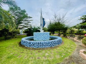 A decorative fountain in a green park featuring a statue of a large jumping fish.

