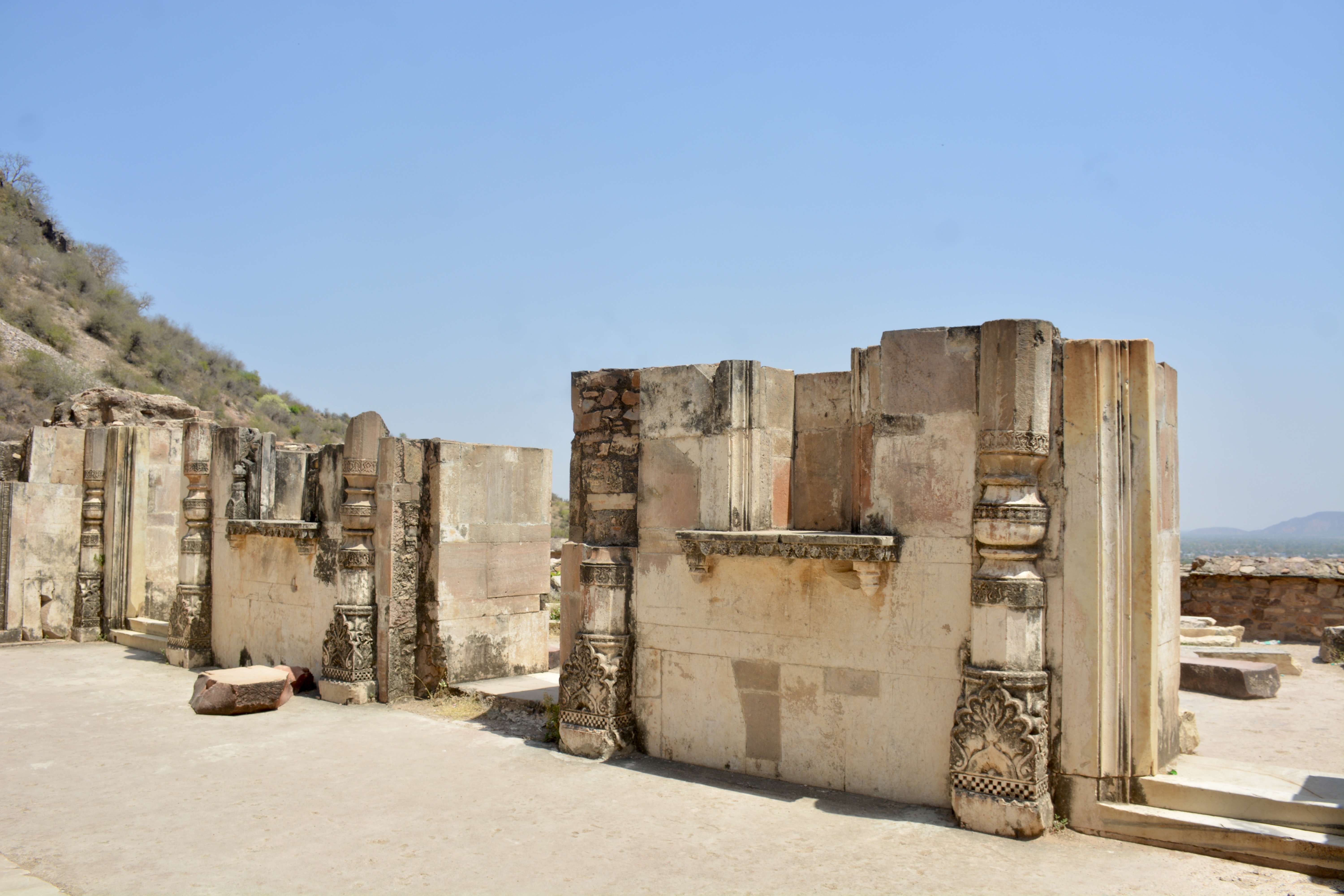 Remains of an old temple at Bhangarh Fort, with intricately carved stone pillars still standing against the blue sky.