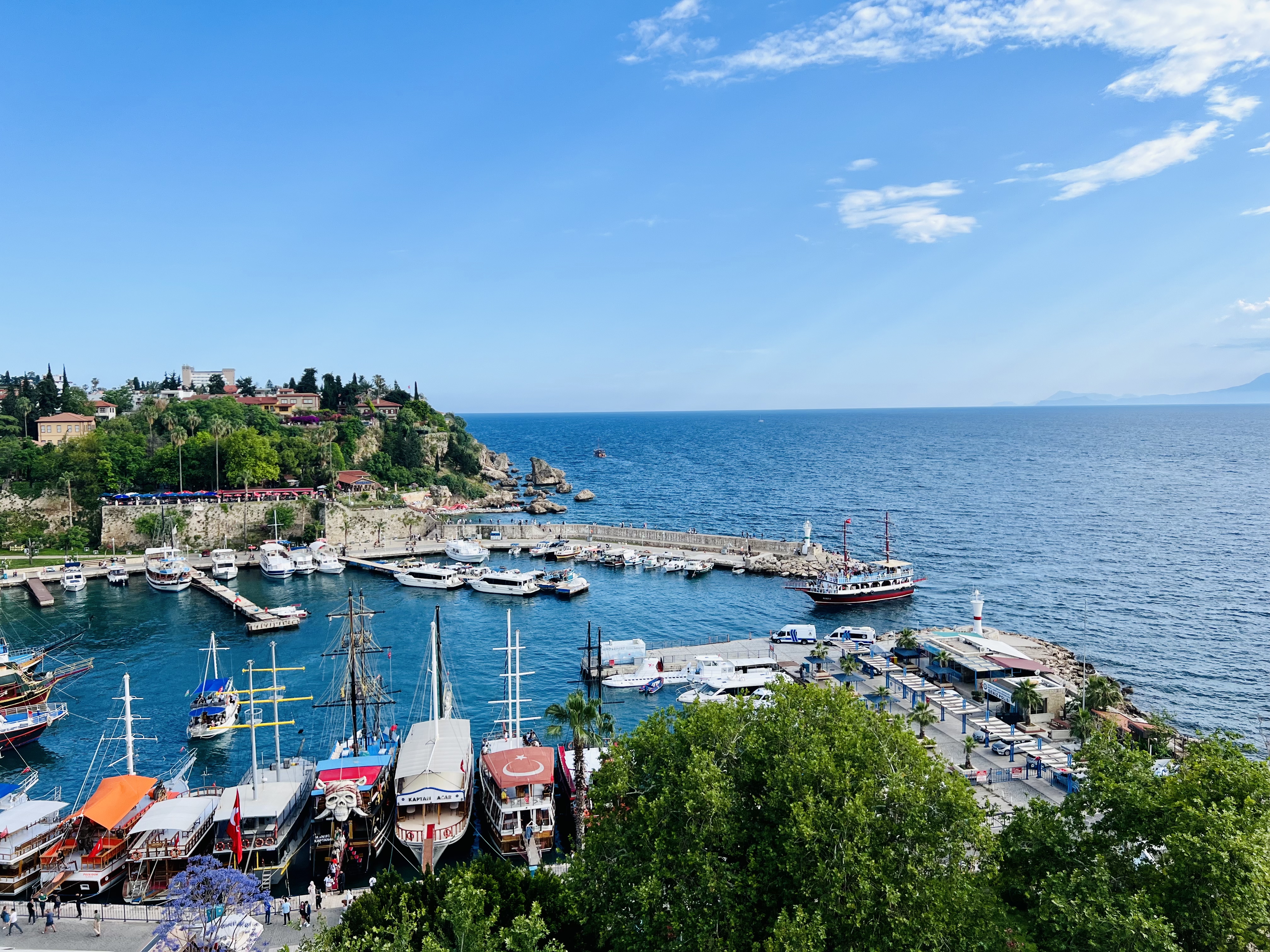 A scenic view of a beautiful harbor in Antalya, Turkey, filled with yachts and tour boats on a sunny day.