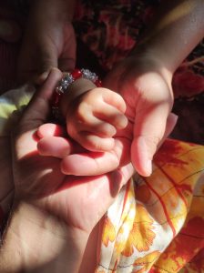 A close-up image of four hands intertwined, showcasing a small child's hand grasping the fingers of an adult hand. 