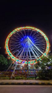 A vibrant Ferris wheel illuminated with colorful lights against a dark night sky at a fairground.