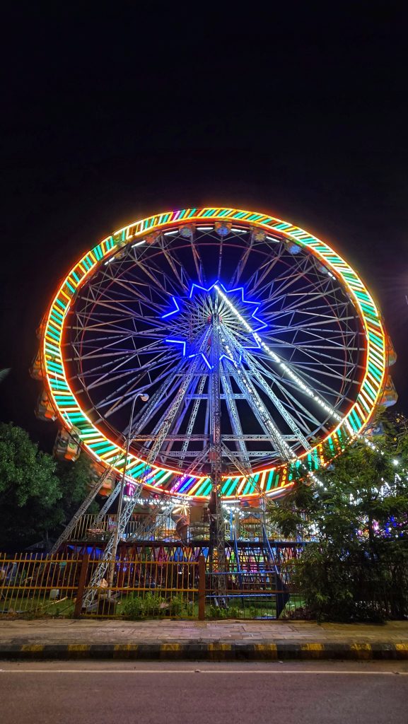 A vibrant Ferris wheel illuminated with colorful lights against a dark night sky at a fairground.