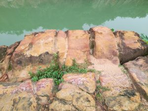 A close-up view of large, multi-colored rocks beside a calm, greenish water surface.