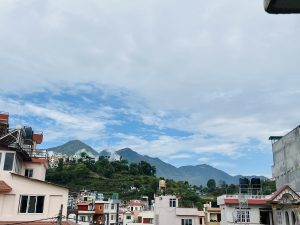 A view of a town with houses in the foreground and a mountain range in the background under a cloudy sky. 