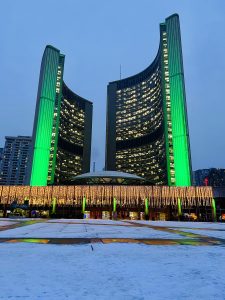 Toronto City Hall at night, lit up with green and yellow lights.
