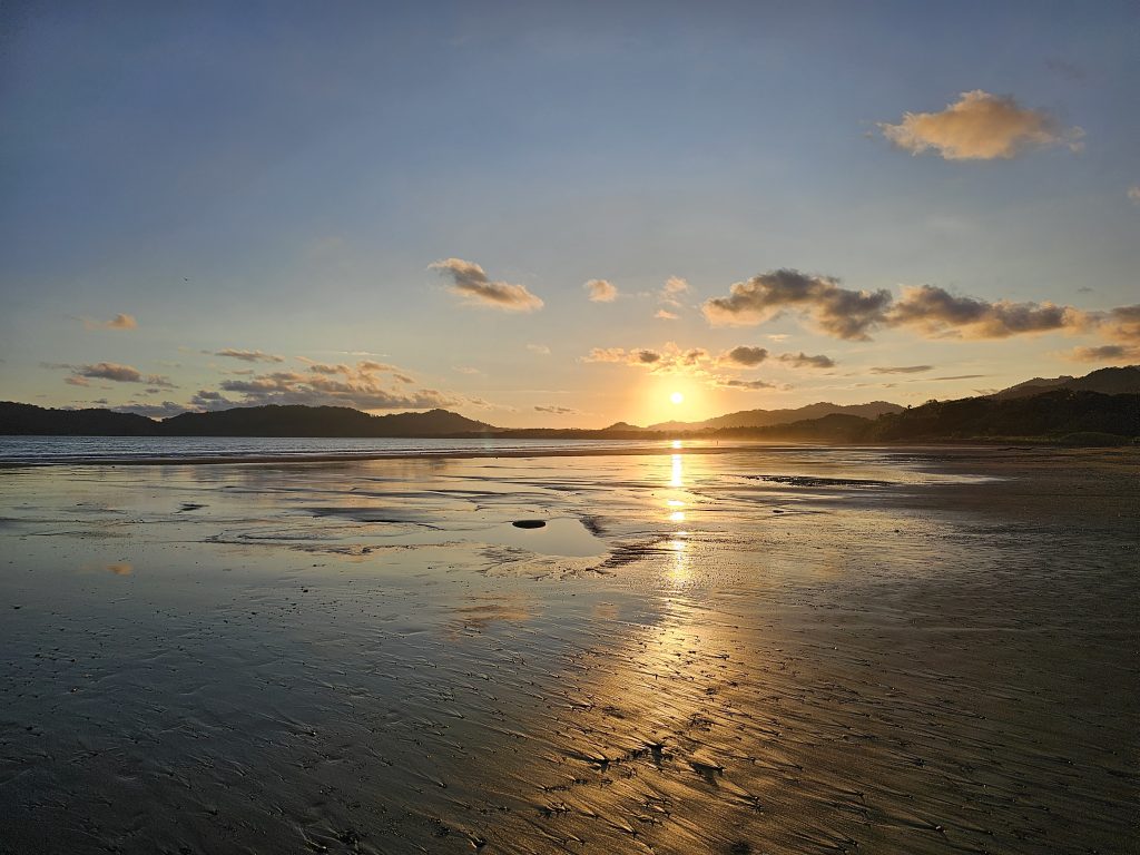 Sunset on the Pacific Coast beach, Costa Rica, with warm light over the water and sand.