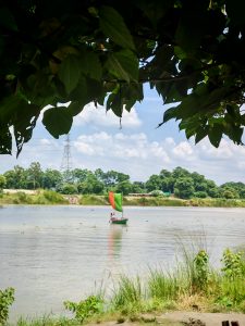 A tranquil river scene features a small boat with a red and green sail navigating the calm waters.