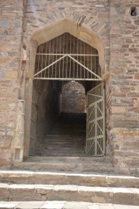 A steep stone staircase leads up through a gated archway, marking one of Bhangarh Fort’s secure entry points.