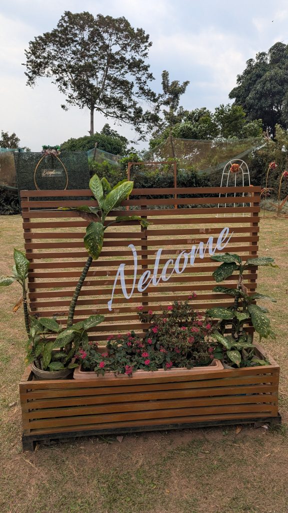 A welcome sign in a garden entrance with several flower pots and trees at its behind. #SummerPhotoContest