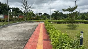 A pathway curves through a landscaped area, featuring a red and orange tiled walkway bordered by lush greenery.