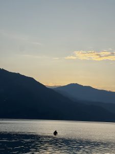 A person on a boat on a calm Fewa lake of Pokhara with mountains in the background at sunset.  