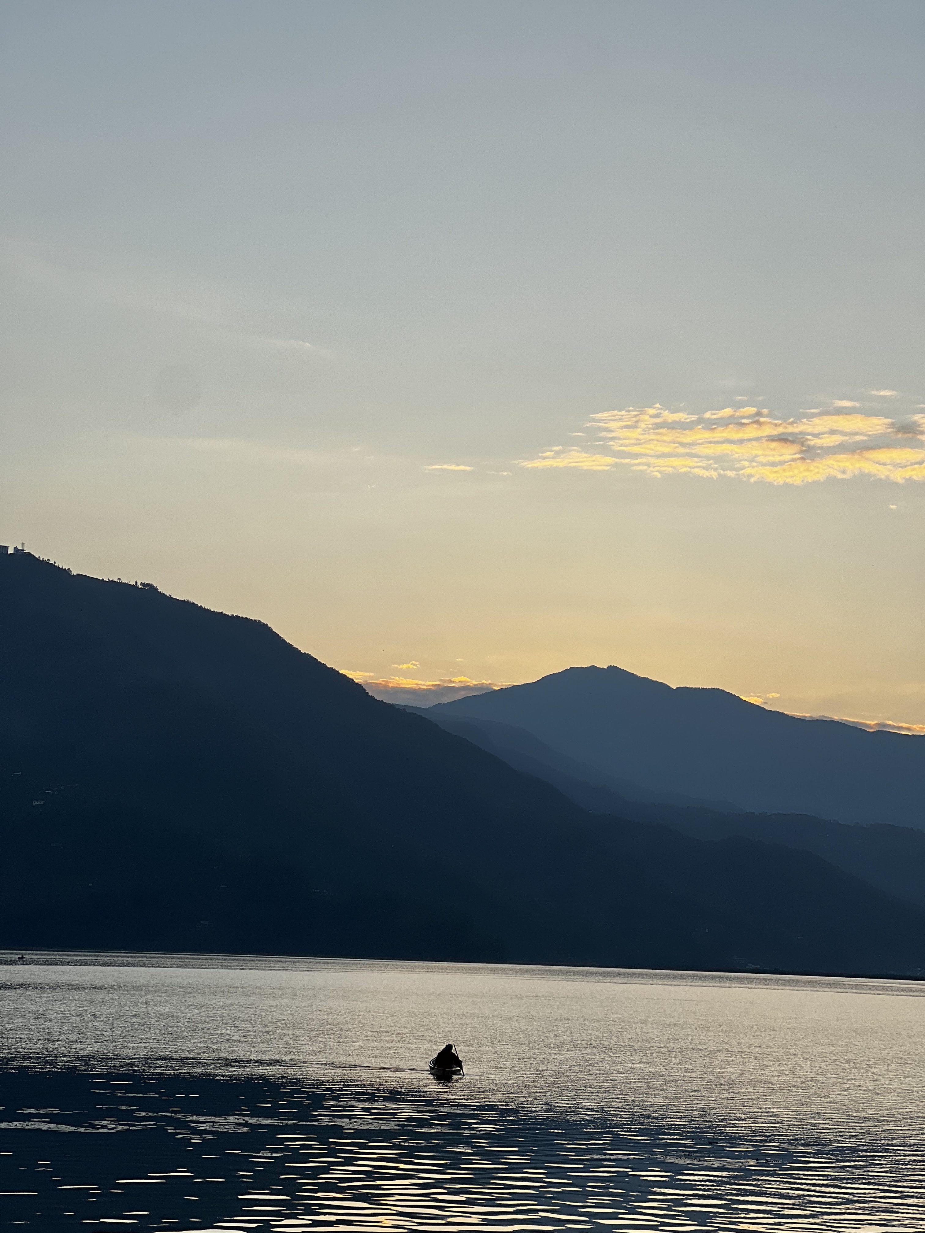 A person on a boat on a calm Fewa lake of Pokhara with mountains in the background at sunset.  