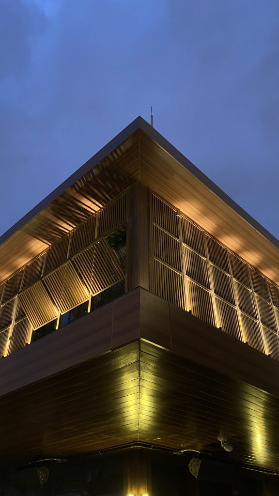 Modern wooden building at Galataport Istanbul, featuring warm ambient lighting and vertical slatted panels, photographed at dusk against a blue evening sky.