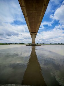 A concrete bridge structure is viewed from below, stretching over a wide body of water.