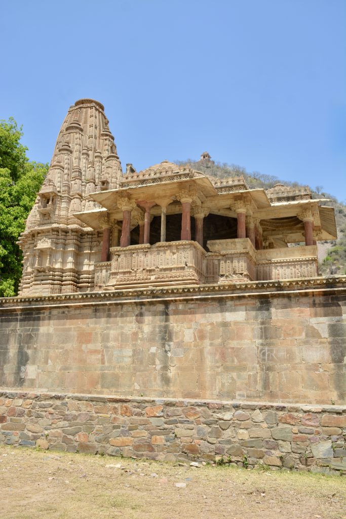 Intricately carved ancient temple at Bhangarh Fort, Rajasthan, with red sandstone pillars and detailed stonework under a clear blue sky.