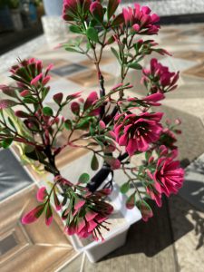 A close-up view of a decorative artificial plant with vibrant pink flowers and green leaves, presented in a white pot.