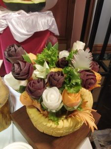 
A colorful vegetable arrangement carved like flowers, presented in a yellow fruit basket with leafy greens, highlighting creative food artistry.