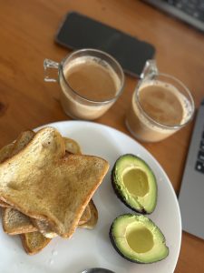 A plate with several slices of toasted bread arranged in a stack, accompanied by two halved avocados with their pits removed. 