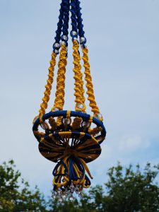 Colorful handmade hanging decor made with twisted blue and yellow cords, decorated with crystal beads, swaying gently in the breeze, captured from an Indian festival in downtown Portland, Oregon.