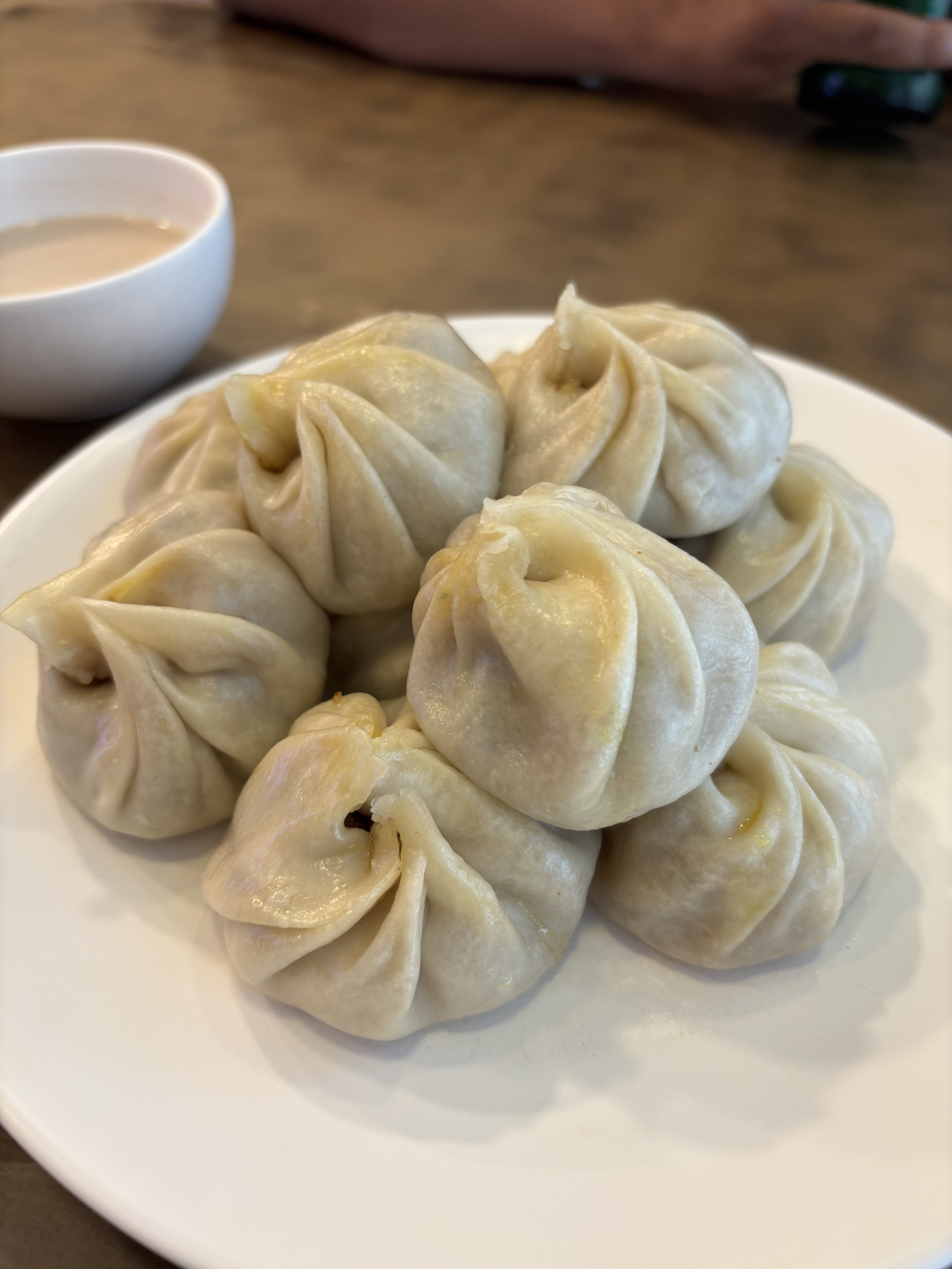 A close-up view of a white plate filled with steamed dumplings, showcasing their pleated tops.