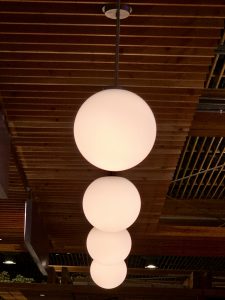 Glowing round pendant lights hang in a line from the wooden ceiling of Portland International Airport. The soft lighting and warm tones highlight the stylish and modern interior of the terminal. 