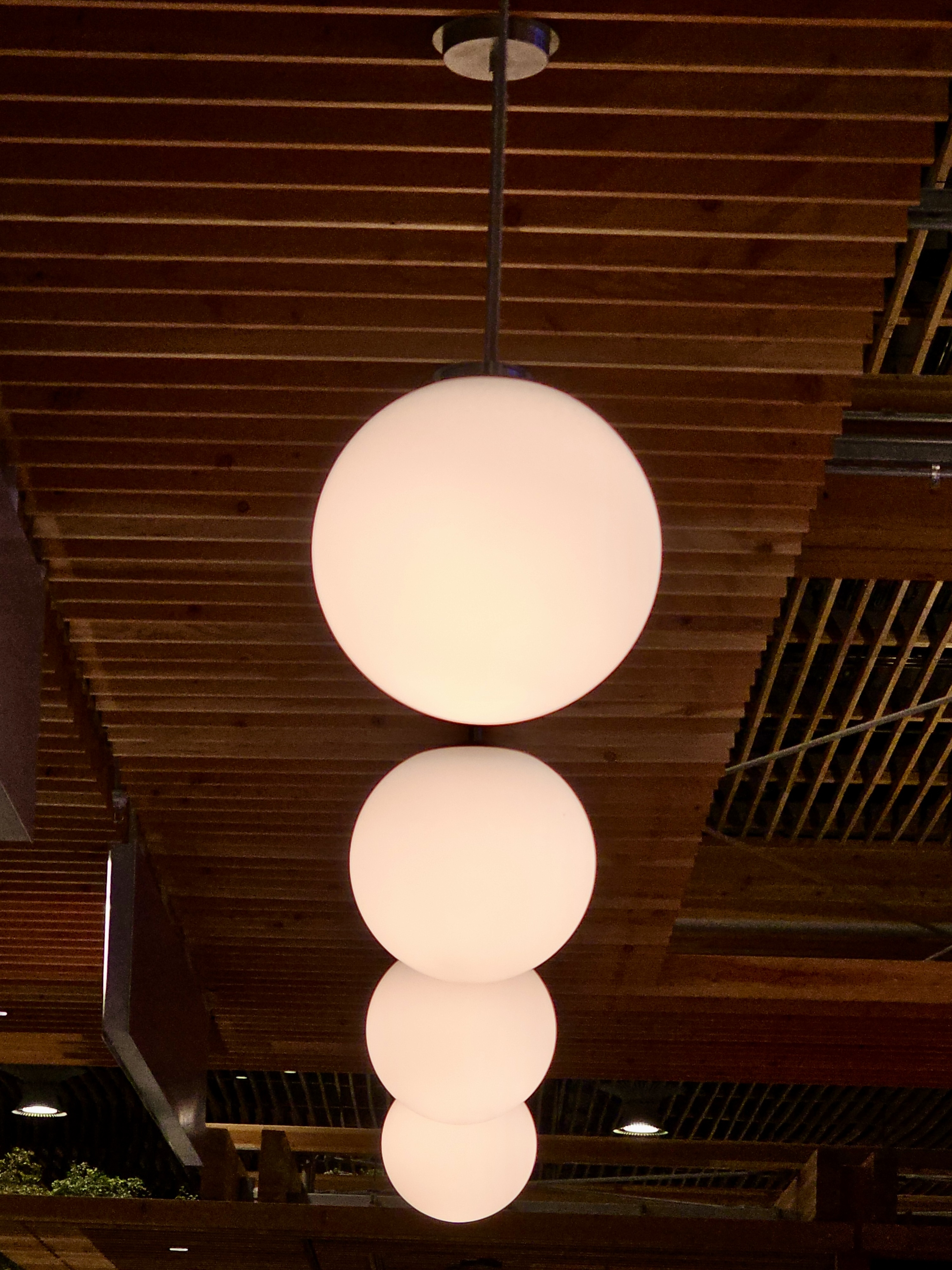 Glowing round pendant lights hang in a line from the wooden ceiling of Portland International Airport. The soft lighting and warm tones highlight the stylish and modern interior of the terminal. 
