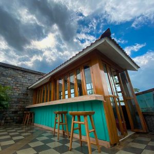 A small, modern structure with large windows and a turquoise accent wall, set against a backdrop of swirling clouds in shades of gray and blue.
