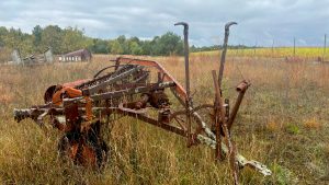 An old fashioned hay rake, rusty and covered in lichens, abandoned in a field.