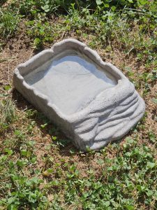 A small stone water bowl placed on dry grass and clover, used for birds or small animals, and captured outdoors in natural light of the Oregon Zoo, Portland.